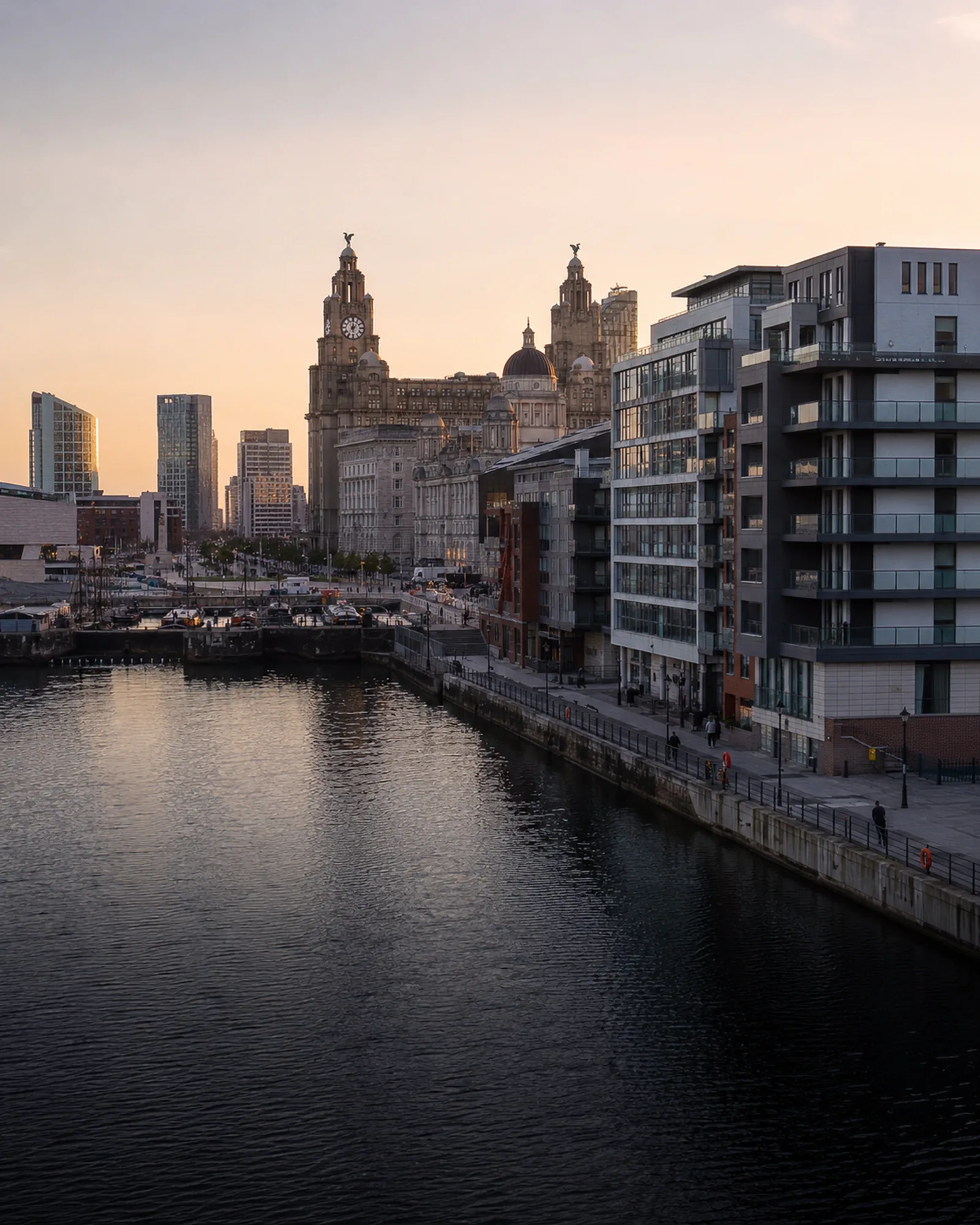 Liverpool's Royal Liver Building and waterfront apartments beside the dock at sunset.