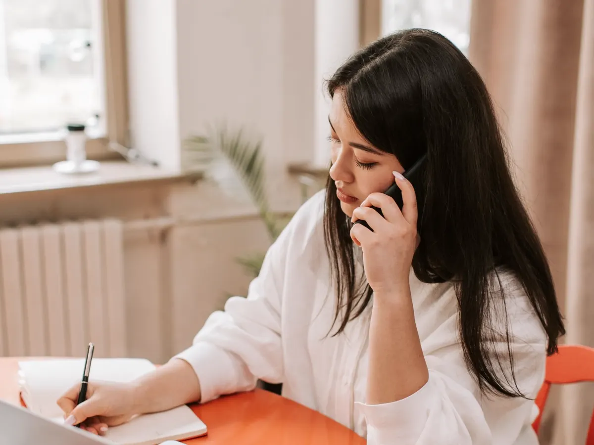A person taking a hospitality call and making notes at a desk