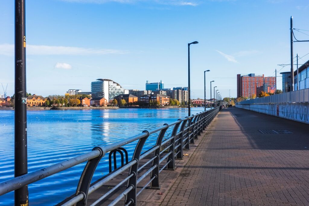 Salford waterfront promenade with Manchester cityscape on a sunny day